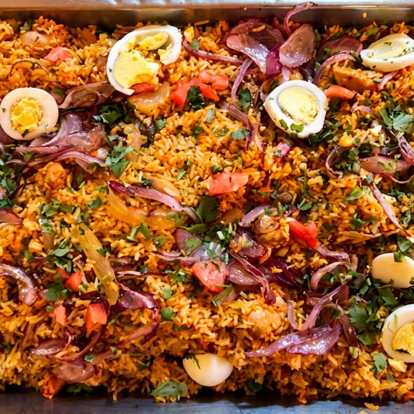 Spiced rice dish with sliced boiled eggs, red onions, and fresh cilantro in a large serving tray.