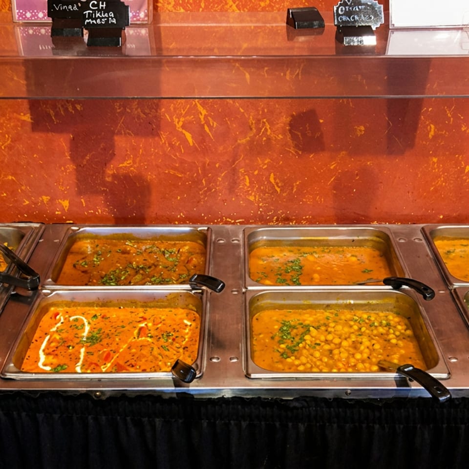Hot buffet line with multiple metal trays filled with colorful curries and vegetable dishes.