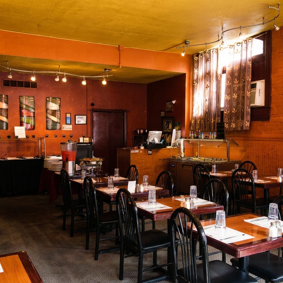 Cozy restaurant dining room with set tables, a buffet, and warm orange walls.
