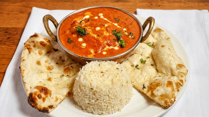 Vibrant orange curry in a brass bowl, served with fluffy rice and two pieces of naan.