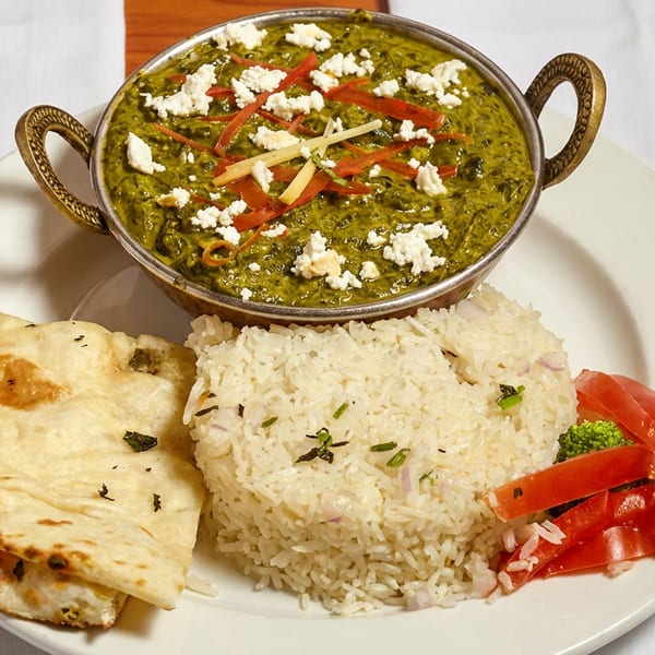 A vibrant Indian meal with palak paneer, fluffy rice, warm naan, and fresh tomato slices.