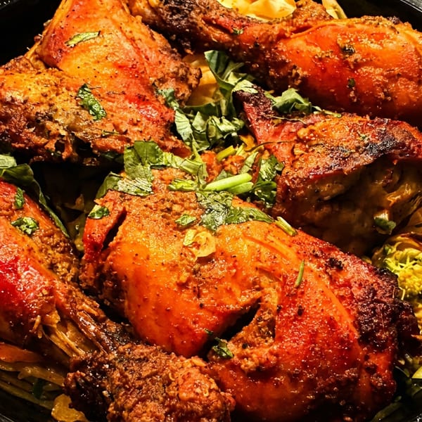 Tandoori chicken pieces garnished with fresh herbs and spices in a black slow cooker.