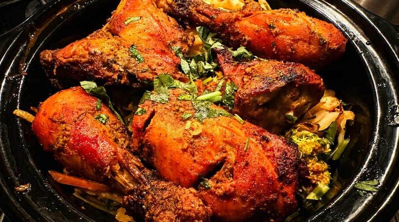 Vibrant red tandoori chicken pieces garnished with fresh herbs in a black cooking pot.